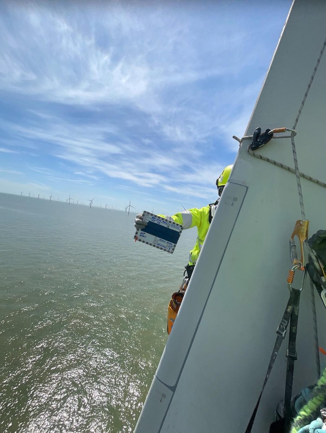 Technik High Work na łopacie turbiny wiatrowej, w tle morska farma wiatrowa